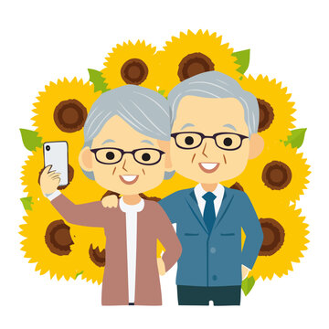 ひまわり畑でスマートフォンを持って自撮りをする仲良しシニア夫婦