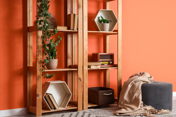 Stylish wooden shelving unit with radio, books, houseplants and decor near orange wall © Pixel-Shot