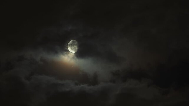 Bright moon breaking through clouds with glowing halo at night