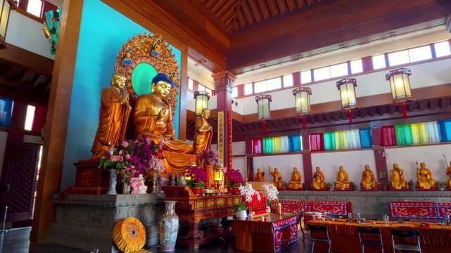 Large golden Buddha statues displayed in a colorful temple interior with lanterns