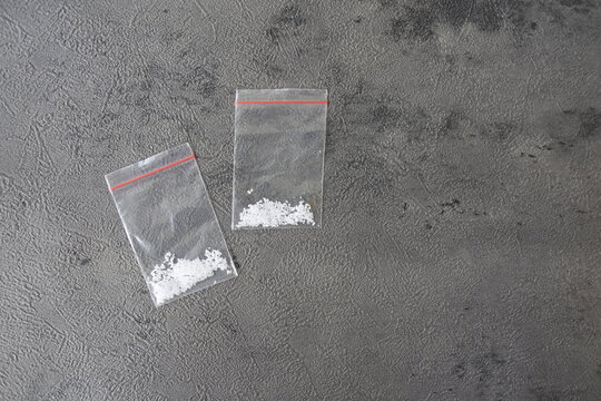 Two small plastic ziplock bags containing white crystalline powder substance on a dark textured background. Concept of illegal drugs, narcotics abuse, or crime evidence.