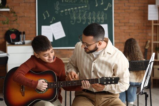 Young boy learning acoustic guitar from male teacher in music class, educational development and creative skill acquisition