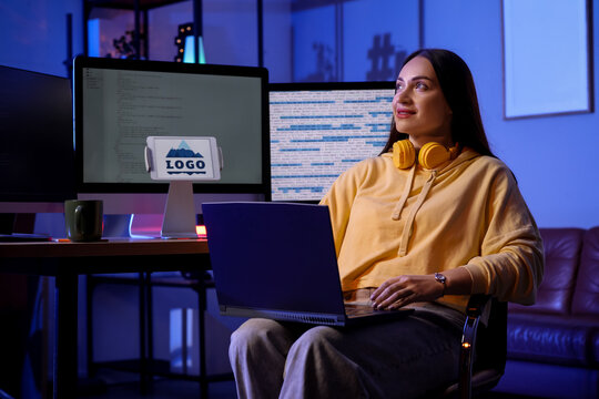 Beautiful young female programmer working with laptop in modern office at night