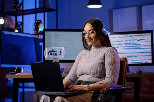 Beautiful young female programmer working with laptop in modern office at night