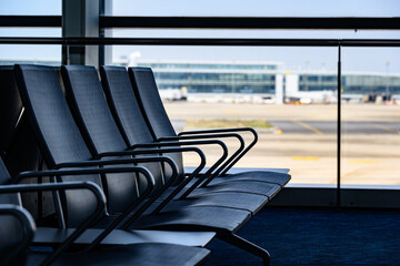 A row of empty modern airport seats in a quiet departure lounge, with the tarmac blurred in the...