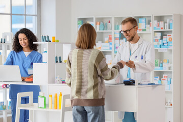 Naklejka premium Pharmacist and pharmacy technician assisting customer with prescription and healthcare products at modern drugstore counter