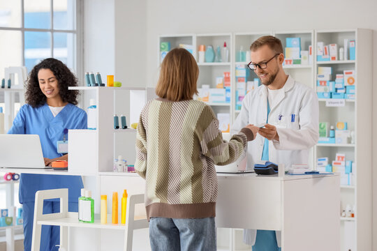 Pharmacist and pharmacy technician assisting customer with prescription and healthcare products at modern drugstore counter