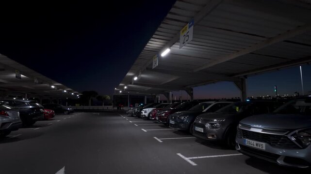 A wide shot captures a large airport parking lot at night. POV