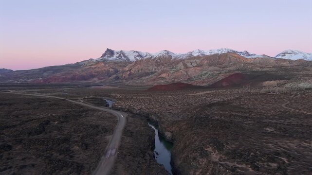 Lonely dirt road bordering deep volcanic canyon in La Payunia, backdropped by pastel purple sunrise skies. Slow, right tracking aerial.