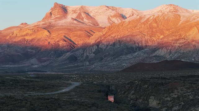 Volcanic canyon beneath snowcapped mountains in La Payunia Reserve Mendoza at sunrise with alpenglow orange reflecting in water