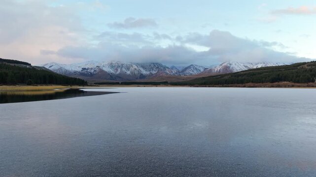 A smooth sideways tracking video moving across the calm water of Laguna La Zeta, revealing snow-capped mountain peaks in Esquel.