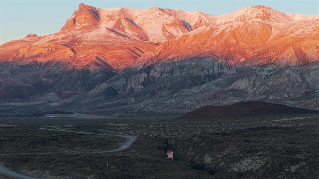 A wide video capturing the golden sunrise light illuminating the snow-dusted volcanic mountain peaks above a vast desert valley in La Payunia Reserve.