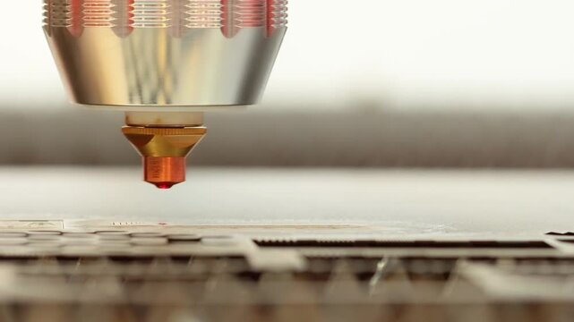 Industrial laser cutter machine cutting metal sheet with sparks in factory workshop.