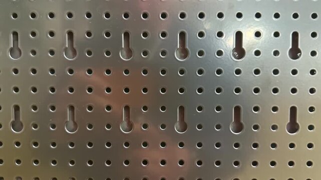 Detailed view of perforated steel panel with keyhole slots and round holes for storage organization