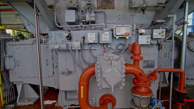 Large industrial gas compressor turbine machinery with orange pipes pressure gauges valves and instrumentation panels inside heavy power plant facility