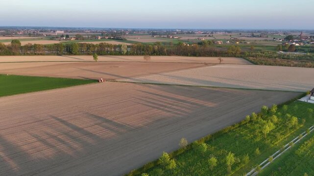 Agricultural machinery prepares soybean fields across the Po Valley in Emilia-Romagna, Italy, revealing large-scale cultivation, fertile farmland and geometric field patterns, drone forward flyover