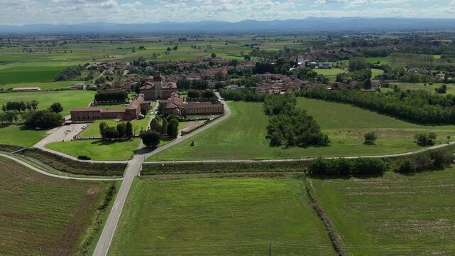 Chignolo Po castle complex with moat, baroque park and village surrounded by green Po Valley farmland, Pavia Lombardy Italy, Dolly left aerial shot