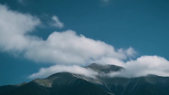 Majestic mountain range with clouds rolling over peaks under blue sky