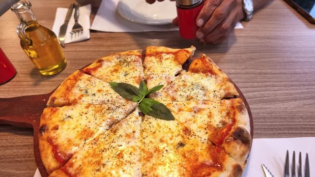 Detailed view of oregano seasoning being added to a freshly baked pizza in a restaurant setting.
