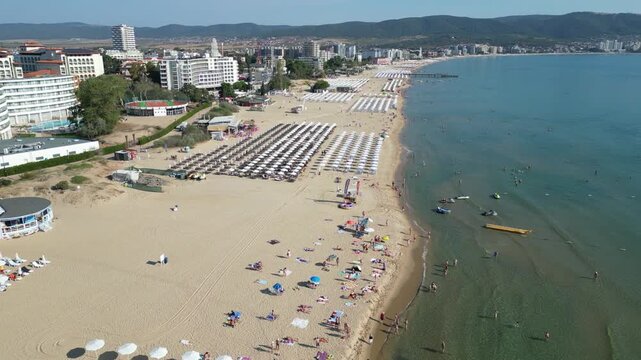 Smooth forward flight along the Sunny Beach coastline with a long beach, rows of umbrellas and visitors by the Black Sea in Bulgaria.