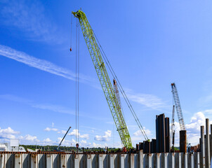 Naklejka premium Port industrial cranes on the river and unloading warehouse on a clear sunny day