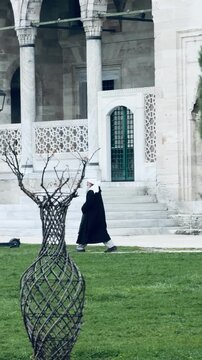 ISTANBUL, TURKEY - MAY 2, 2026: Elderly Muslim man with beard wearing traditional caftan and turban walking past historic stone arches in courtyard of Suleymaniye Mosque. Ottoman style culture.