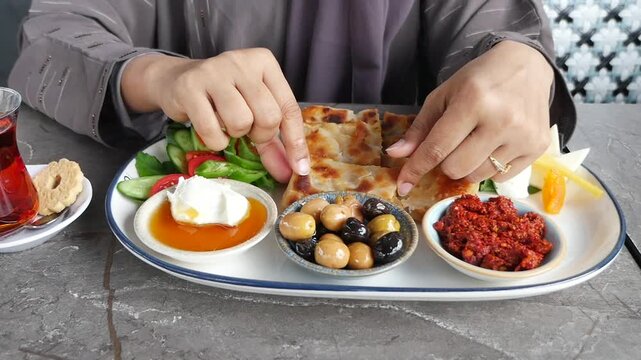 a woman enjoying traditional Turkish breakfast spread, featuring diverse dishes like olives, cheeses, and freshly baked bread