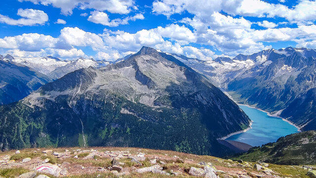 Alpine landscape near Olperer Hutte in Austria featuring high mountains and turquoise Schlegeis reservoir lake under blue sky with white clouds