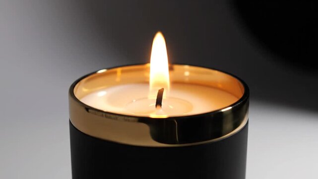 Scented candle burning inside an elegant black and gold luxury jar.