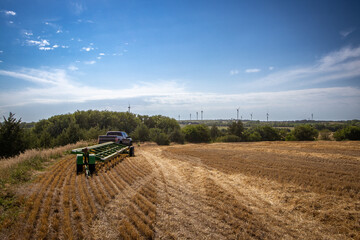 Naklejka premium Agricultural Equipment Overlooking Harvested Field and Distant Wind Farm