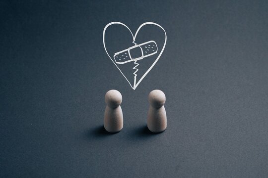 Two wooden figures face a broken heart with a bandage