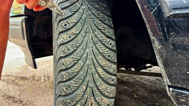 Man uses hand tool to extract stuck stones and dirt from stud holes on winter car tire tread during maintenance process outdoors