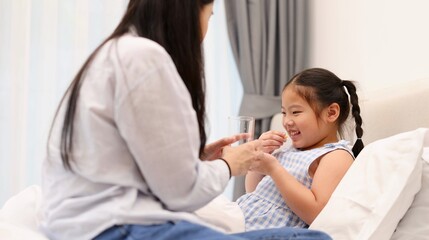 Obraz premium Asian Mother Helping Her Sick Daughter Take Medicine in Bed