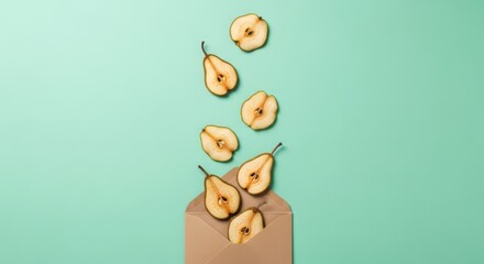 Fototapeta premium Flat lay of fresh pear slices falling into a brown paper envelope on a pastel green background
