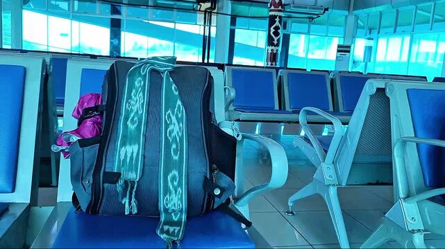 Close-up of a tourist rucksack with local ethnic textile on an empty blue bench in a transit terminal lobby during a trip.