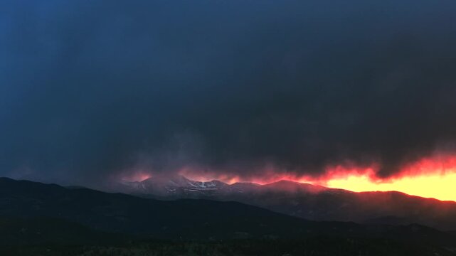 Sunset golden hour vibrant orange dark thunderstorm rain cloud fire orange sky Mount Blue Sky aerial drone Colorado Rocky Mountains Spring snow covered Mount Evans Wilderness front range peaks forward
