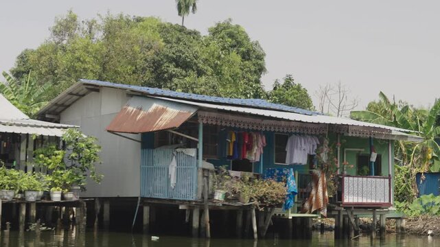 A traditional stilt house stands above the water along a canal in Bangkok, Thailand. The colorful riverside home reflects everyday life in the city's waterfront communities, where canals remain an imp