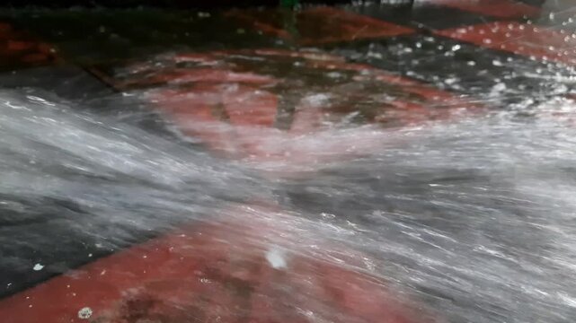 Highpressure water jet spraying on a tiled floor, creating a dynamic splash and cleaning effect, closeup view of water flow on textured surface