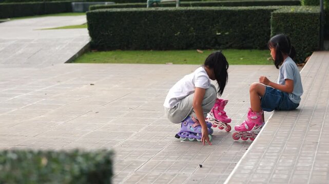 Happy Asian children girls exercising balance and rollerskating together inside public park meadow. Cute young friends playing joyful sport hobby lifestyle view outdoor project development.