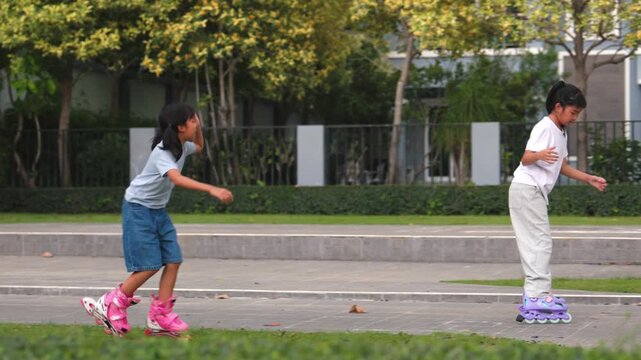 Cute young Asian children girls rollerskating and balancing together inside summer public park green field. Happy classmates enjoying joyful outdoor exercise space process.