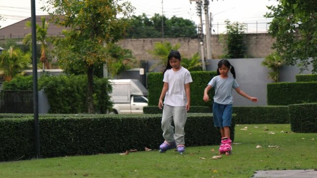 Happy Asian children girls exercising balance and rollerskating together inside public park meadow. Cute young friends playing joyful sport hobby lifestyle shot outdoor project development.