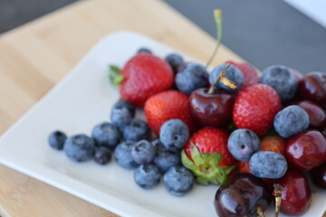 Close up of fresh ripe strawberries and blueberries. Fresh summer berries including strawberries, blueberries and sweet cherries served on a white square plate, top view. © Nadiia