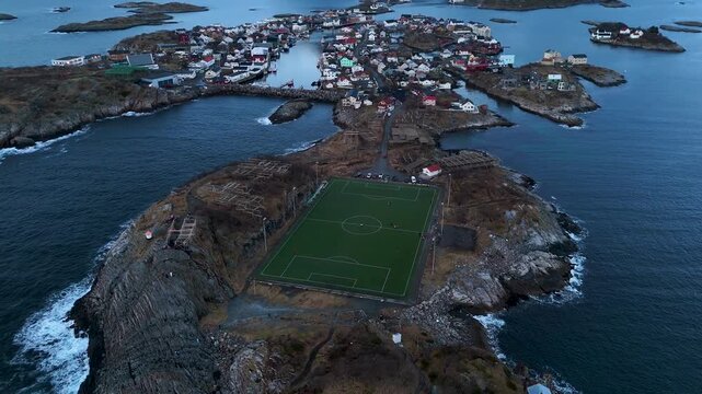 Amazing aerial shot of Henningsvaer stadion (football pitch), revealing the whole Fishing Village and snowy mountains, Lofoten, Norway, at blue hour Horizontal tilt reveal footage