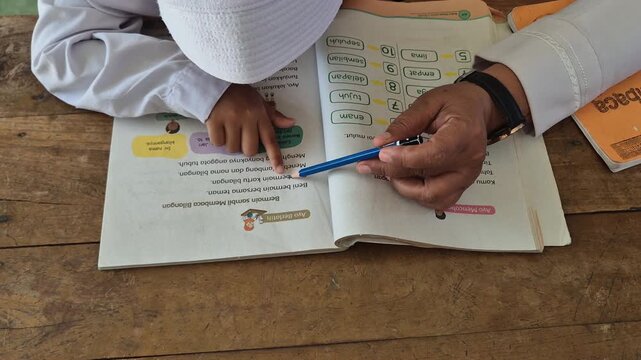 Teacher Guiding Young Muslim Student Reading and Counting in Textbook