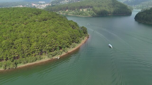 Low Altitude Drone Tracking Tourist Boat on Tuyen Lam Lake With Pine Forest Shoreline in Da Lat, Vietnam