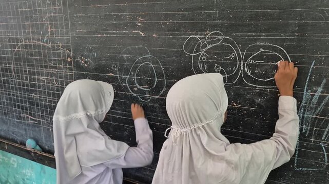 Creative Muslim Elementary School Student Drawing with Chalk on Blackboard in Classroom