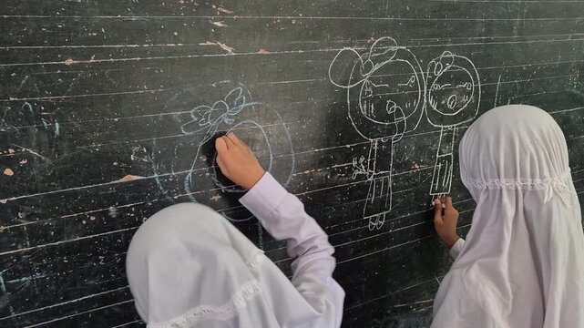 Creative Muslim Elementary School Student Drawing with Chalk on Blackboard in Classroom