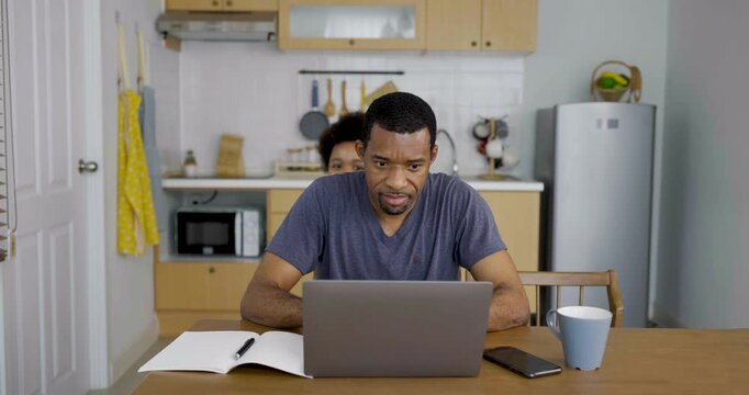 Portrait of focused father using gadget laptop at kitchen table while young child play beside him, showing remote work, parenting, and Single dad family life.