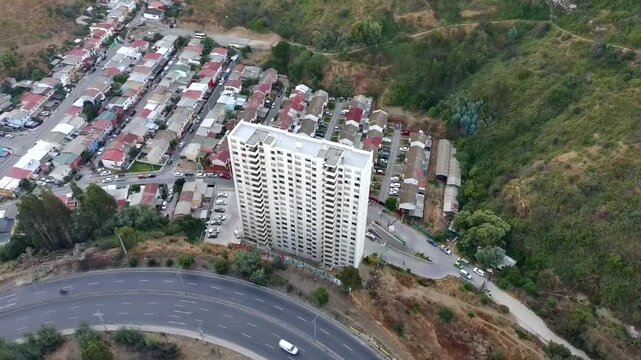 Drone footage of a residential high-rise building, hillside houses, urban roads and curved highway, showing city housing, transportation and urban development.