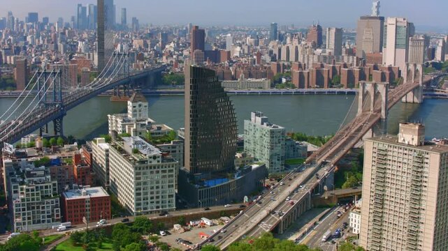 Brooklyn bridge and Manhattan bridge aerial view during sunny day in New York City with East River and urban architecture featuring busy traffic on highway.